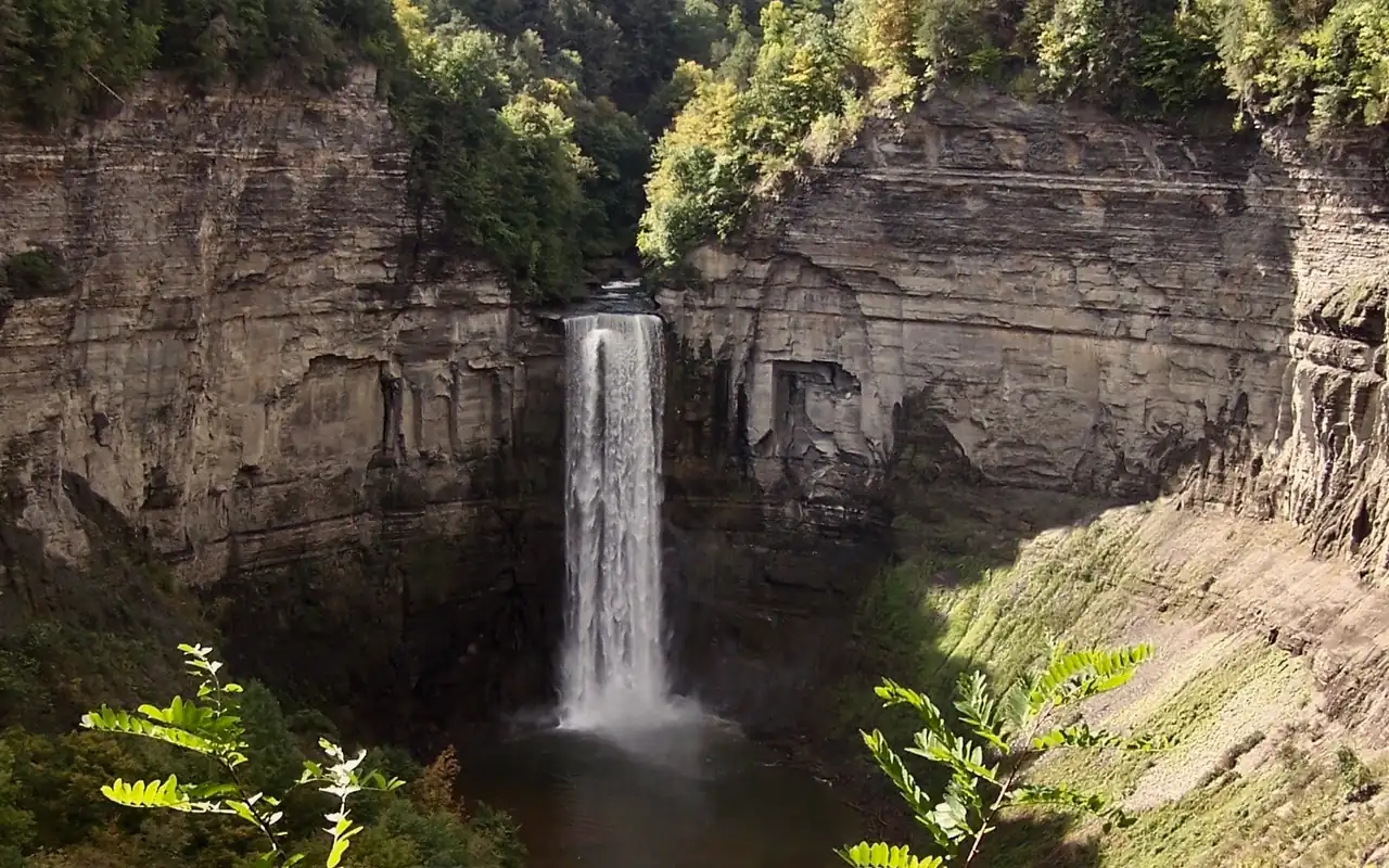A tall waterfall dropping into a pool in a deep, wooded rock gorge.